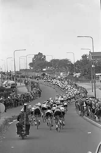 Het peloton slingert zich tussen hagen van publiek een heuvel op