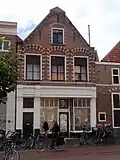 Voorheen trapgevel van Haarlems type, bogen boven vensters op console rustend, engelen en leeuwenmaskers. Beneden verbouwd