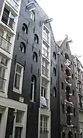 Dubbel pakhuis met trapeziumgevels aan voor- en achterzijde beide met gevelsteen met hand, bij de laatste met een grote kroon erboven