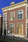 Pand ter breedte van drie vensterassen onder half schilddak. Parterre en verdieping. Lijstgevel met in de architraaf gesneden ornament in late Lod. XVI-stijl