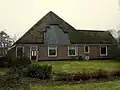Stolphoeve met dwars uitgebouwd wooneind, eindigend tegen gevel met houten top. Kelder tussen wooneind en dwarseind. Gebogen bovenraamdorpels, de roeden verwijderd uit de onderramen
