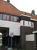 Poortgebouw met twee winkels met bovenwoningen, met veel hout zoals de zware kolommen in poort, bouwstijl Amsterdamse School, ligging aan Purmerweg centraal deel van Tuindorp Nieuwendam