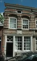 Huis onder schilddak en met een tot lijstgevel afgeknotte gevel van het 'Dordtse' type, met natuurstenen banden en waterlijsten, tegen de verdieping geprofileerde korfbogige ontlastingsbogen