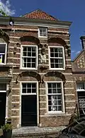 Huis onder schilddak en met een tot lijstgevel afgeknotte gevel van het 'Dordtse' type, met natuurstenen banden, geprofileerde bakstenen waterlijst, geprofileerde korfbogige ontlastingsbogen