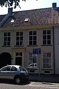 Pand, ter breedte van vier vensterassen met lijstgevel, geprofileerde houten vensteromlijstingen, deurpilasters met hoofdgestel en links poort naar het binnenhof van het